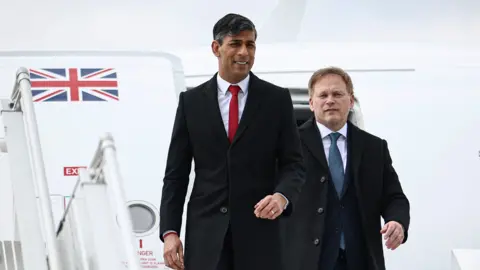 Getty Images Rishi Sunak and Grant Shapps emerge from an aeroplane with a Union Flag emblazoned on the open hatch behind them