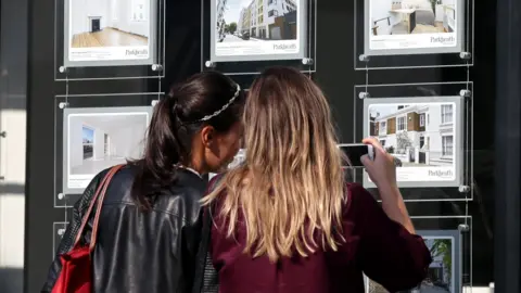 PA Media Two young women look at an estate agent's window display