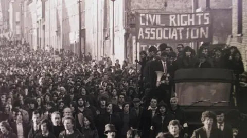 PA Media A black and white image of crowds gathered. People on the back of a truck are holding up a banner reading: "CIVIL RIGHTS ASSOCIATION".