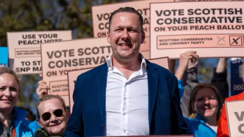 PA Media Russell Findlay standing in front of a number of supporters holding up peach ballot papers.