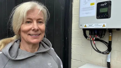 Julie Clague stands next to the battery system at the back of her home.