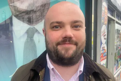 Reuters A bald man with a moustache and beard. It is a head and shoulders shot, and he is stood outside.